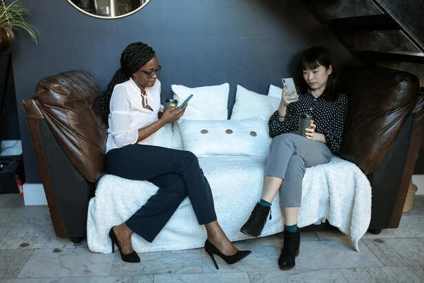 Two Friends Looking at Their Phones During Conversation